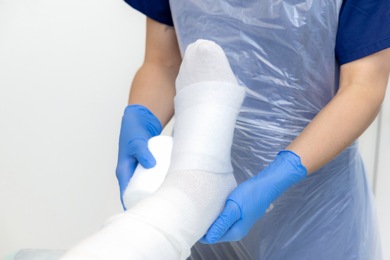 Person verbindet Bein mit einer Mullbinde