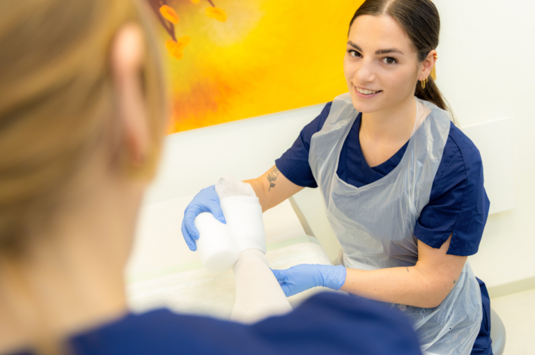 Frau verbindet Bein mit einer Mullbinde, schaut in die Kamera