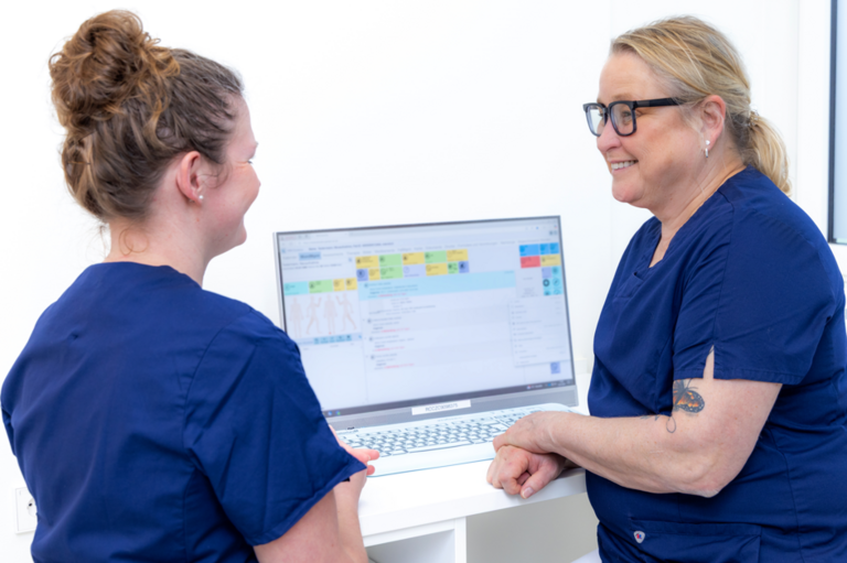 Zwei Frauen sprechen miteinander und sitzen vor einem Computer