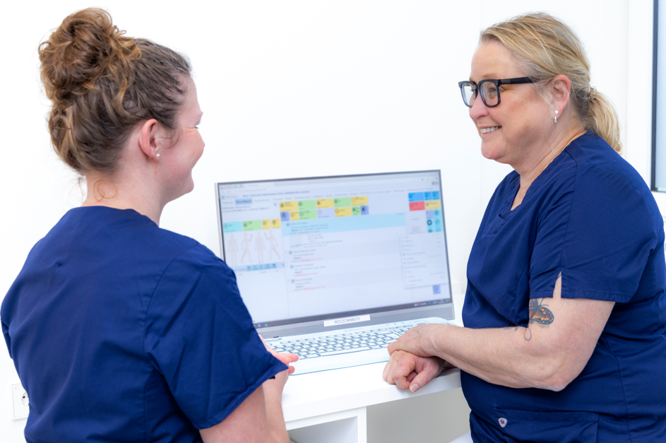 Zwei Frauen sprechen miteinander und sitzen vor einem Computer